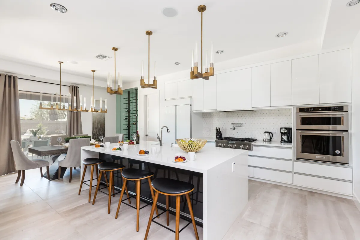 A contemporary kitchen view highlighting a central island with comfortable seating and hanging light fixtures, seamlessly connected to a formal dining area in the background. The setup is ideal for family meals, entertaining guests, and facilitating conversation between kitchen and dining spaces.