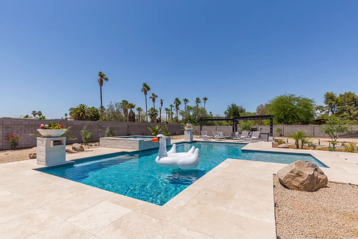 A sparkling swimming pool is the centerpiece, with an inflatable swan float adding a playful touch. The landscaped garden and comfortable patio seating suggest relaxation after games, and the Arizona sky in the background underscores the outdoor lifestyle.