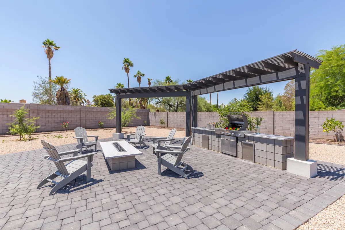 An inviting outdoor dining area set beneath a pergola, complete with a spacious grill station and a paved patio perfect for large group celebrations or relaxed poolside brunches. The setting evokes a sense of sociability and alfresco enjoyment.