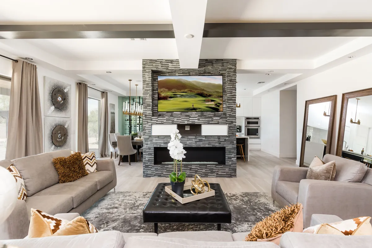 A cozy living room featuring a large television mounted on a striking stone feature wall, a modern coffee table adorned with decorative pieces, and an inviting arrangement of comfortable seating. Sunlight streams in, creating an airy, welcoming atmosphere ideal for socializing or relaxing with family and friends.