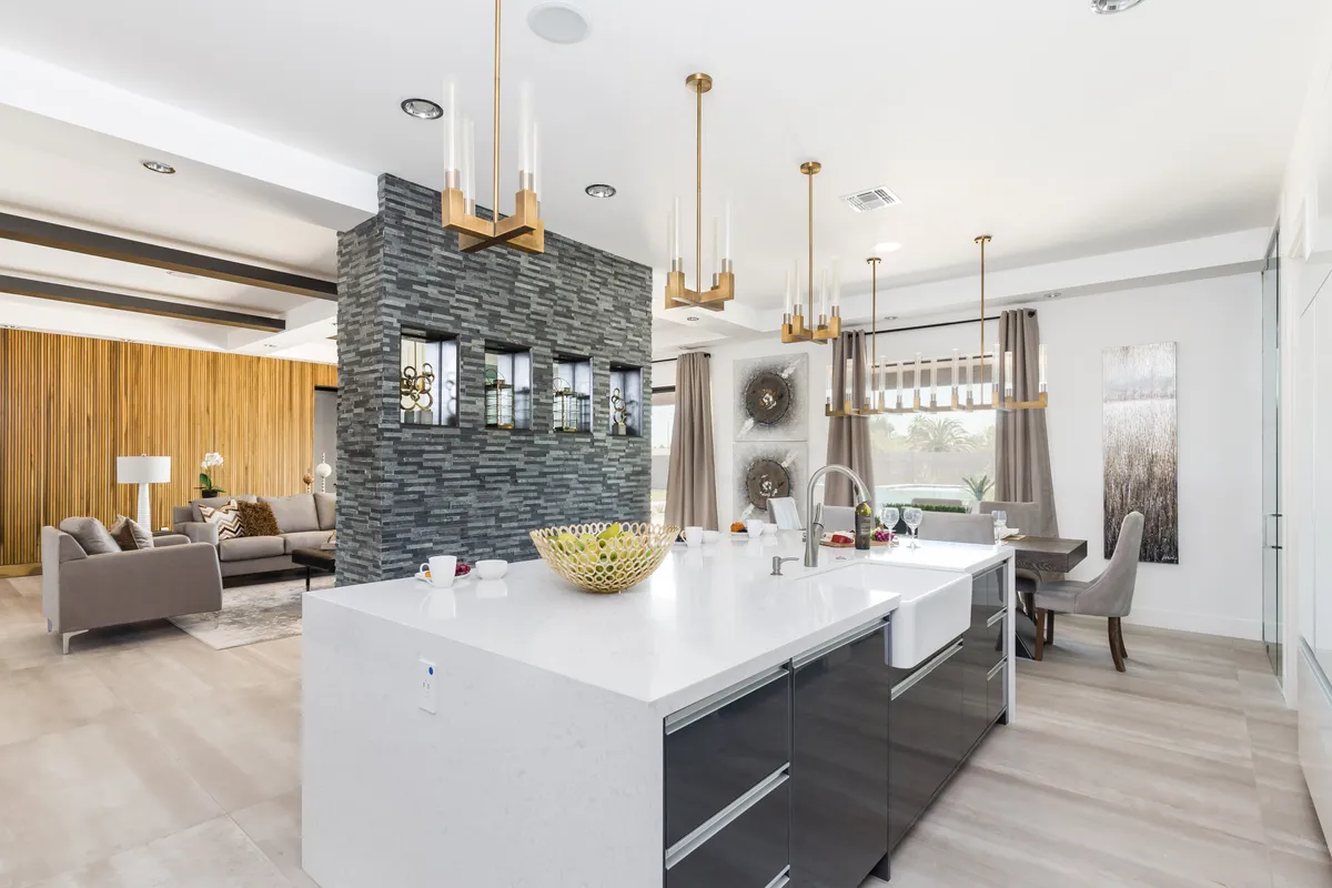 A bright, modern interior blending the living area, a central kitchen island, elegant chandeliers, and a stone wall feature. The image captures multiple activity zones—spaces for cooking, dining, and relaxing—unified under a cozy yet stylish design.