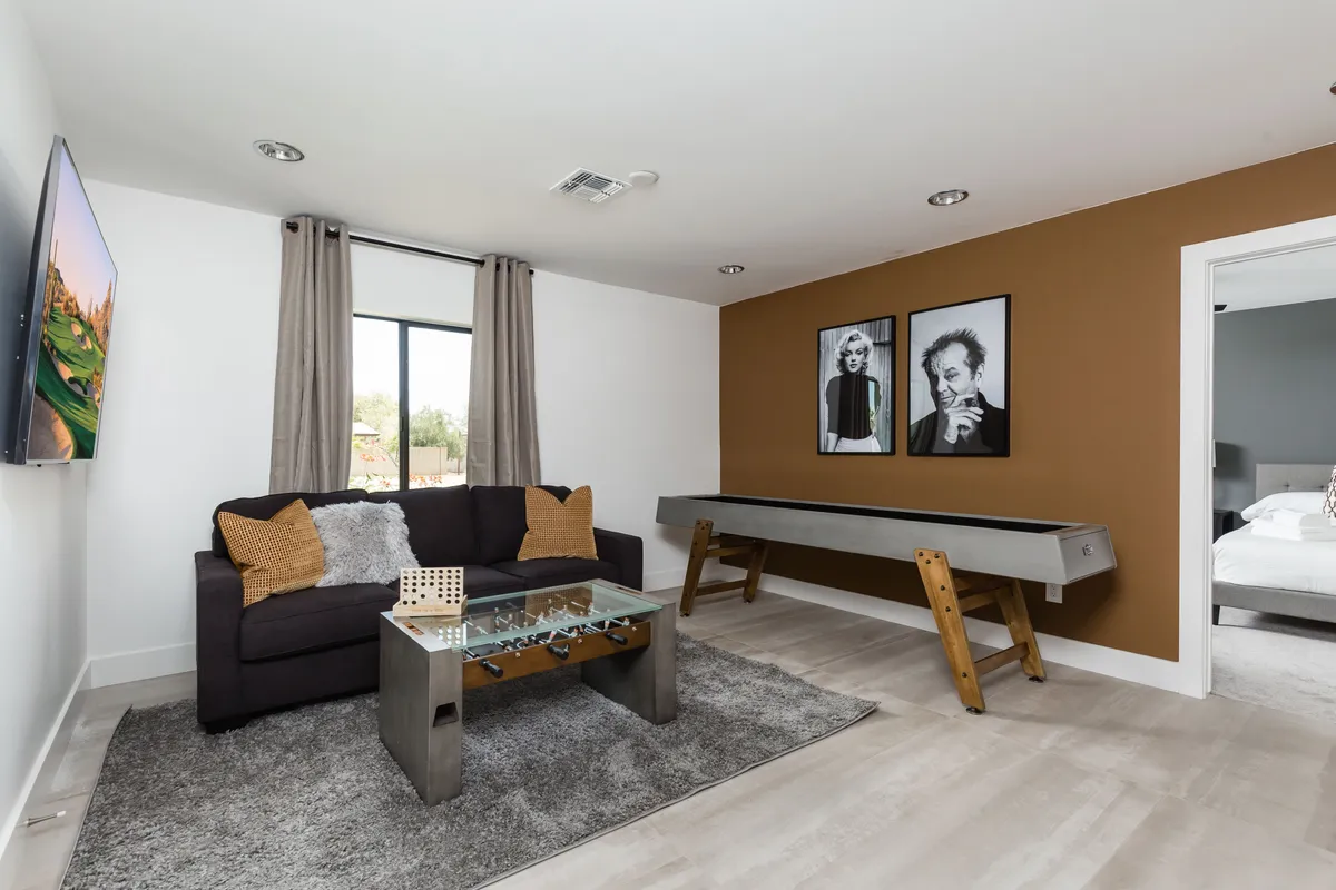 A vibrant game room with a sofa, artwork on the wall, glass coffee table, and a pool table, blending relaxation with entertainment. The room is inviting and stylish, perfect for socializing, game nights, or accommodating extra guests via the sofa bed.