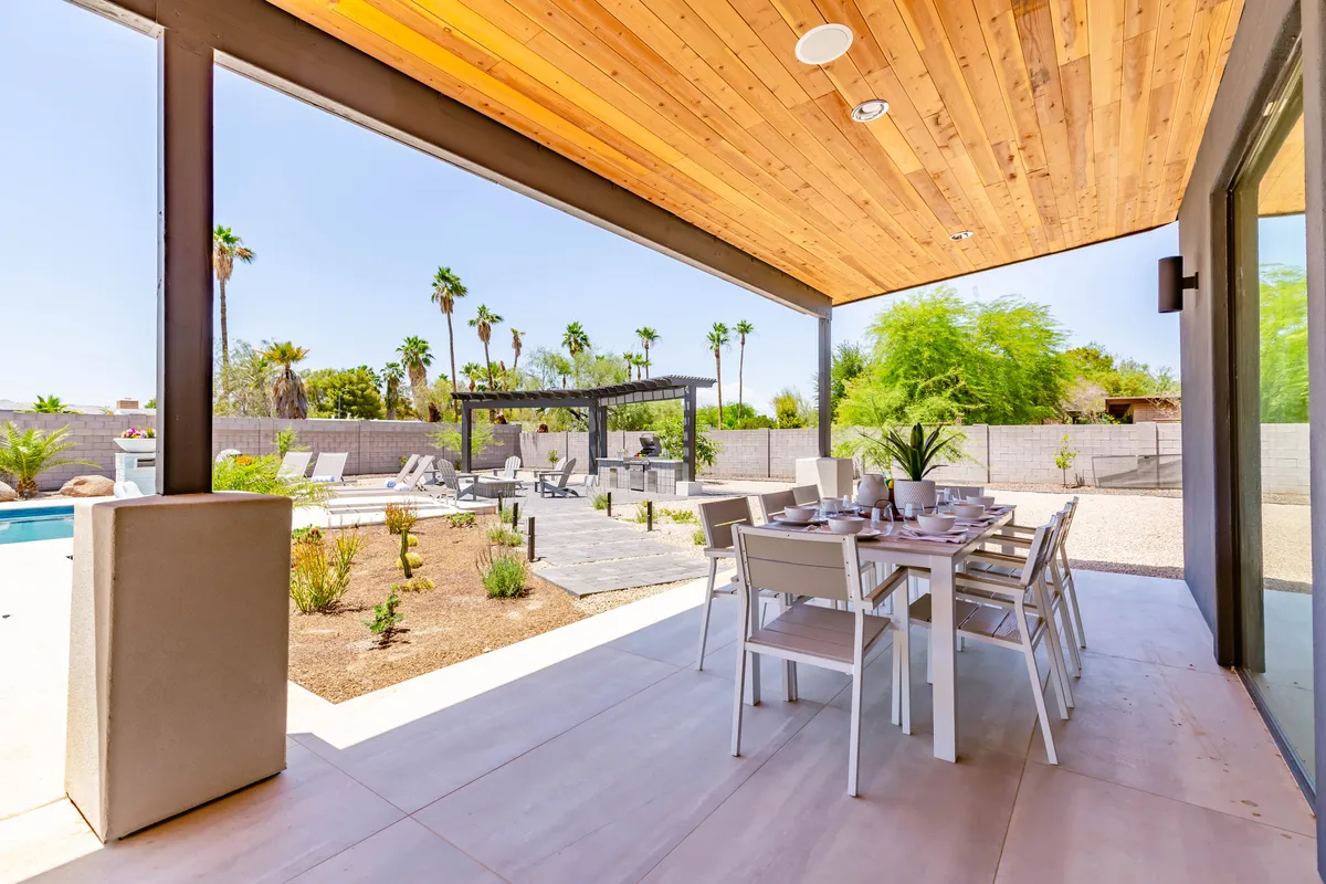 An inviting outdoor dining area set beside a shimmering pool, surrounded by palm trees and lush landscaping. The scene includes a table set for meals, comfortable seating, and a serene ambiance ideal for barbecues or sunset gatherings.